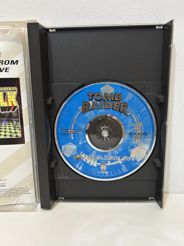 Disco de Tomb Raider para Sega Saturn dentro da caixa aberta, com material impresso ao lado